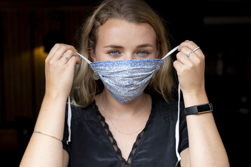 Portrait of young blond woman putting on blue face mask.