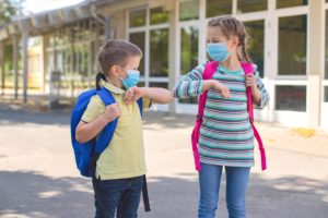 Children, a boy and a girl, wearing masks, greet their elbows on the street in the schoolyard due to the coronavirus epidemic. Distance observance, new school reality. Children, a boy and a girl, wearing masks, greet their elbows on the street in the schoolyard due to the coronavirus epidemic. Distance observance, new school reality.